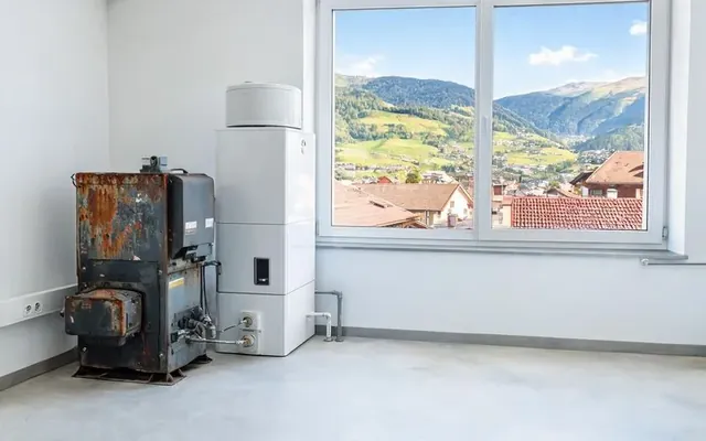 Chauffe-eau thermodynamique moderne dans un local technique de maison suisse à côté d'un ancien boiler électrique