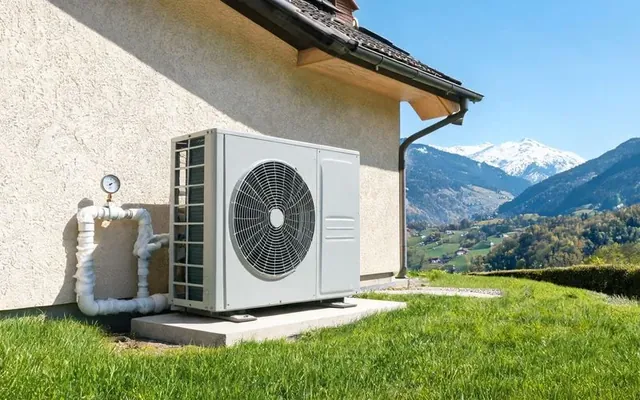 Unité extérieure d'une pompe à chaleur air-eau surdimensionnée sur une dalle contre une maison suisse à Sion